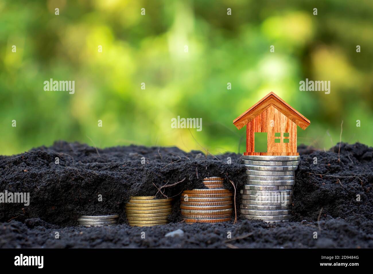 El modelo de la casa de madera en la moneda contiene monedas que crecen en el suelo con el concepto de ahorro de dinero, fondo verde de la naturaleza. Foto de stock