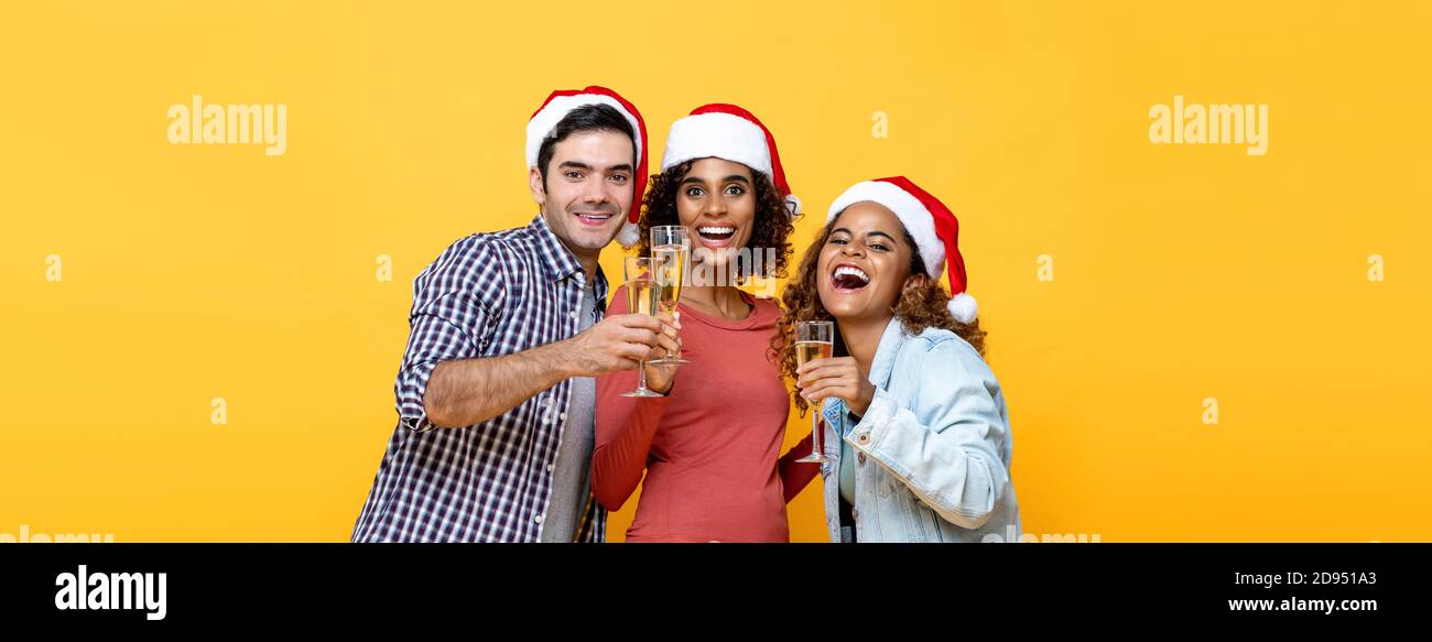 Grupo de amigos diversos bebiendo champán celebrando la Navidad en amarillo estudio de color de fondo aislado Foto de stock