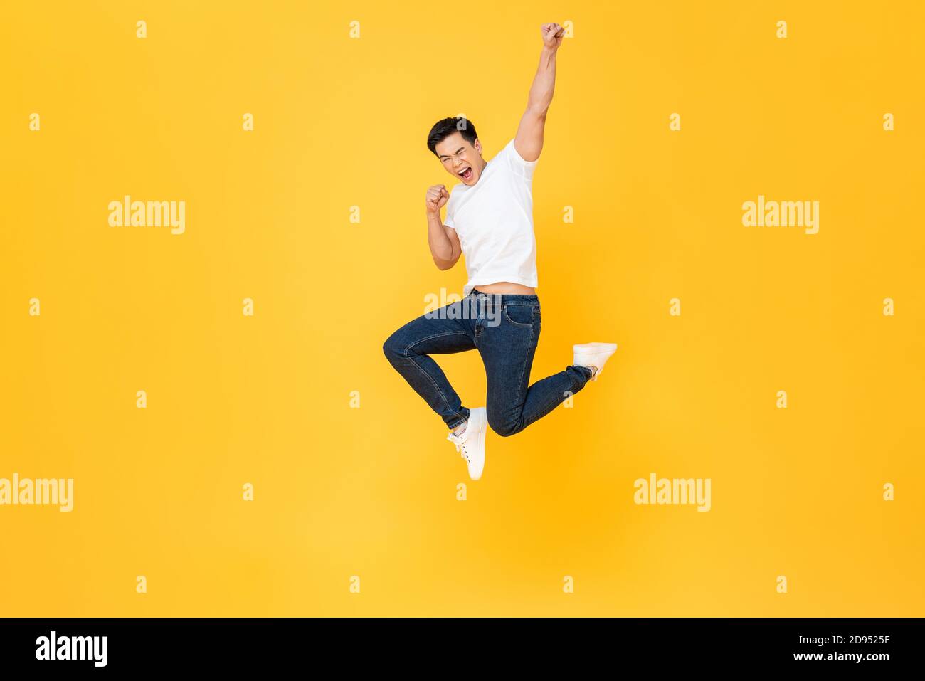 Joven y enérgico hombre asiático saltando y levantando su puño aislado sobre fondo de color amarillo Foto de stock