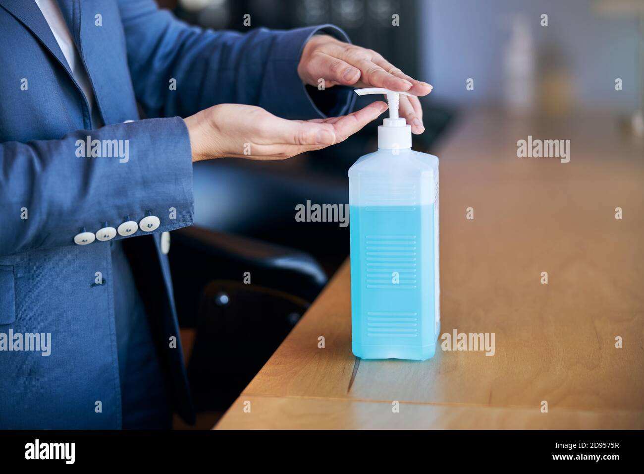 Mujer rociando desinfectante a base de alcohol a mano en el trabajo Foto de stock