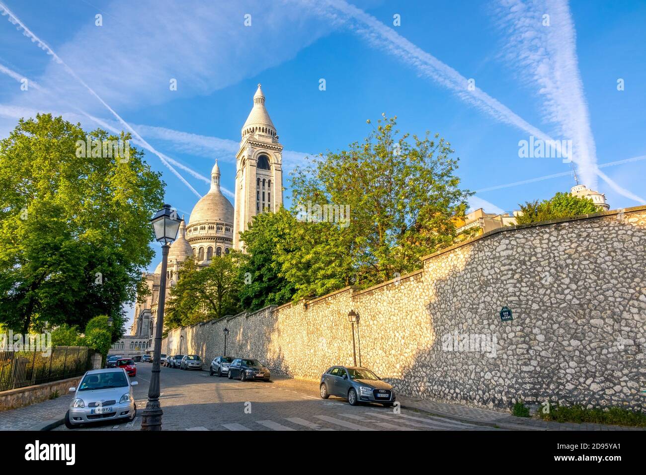 Francia. Soleado día de verano en París. Los tejados de la abadía de Sacre Coeur contra el cielo azul. Varios coches aparcados en una calle adoquinada. Foto de stock