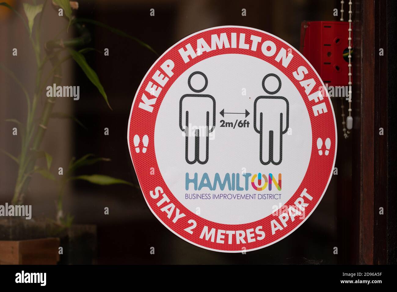 Mantenga a Hamilton seguro manténgase a 2 metros de distancia signo fuera de la tienda en Hamilton, South Lanarkshire, Escocia, Reino Unido durante las medidas locales coronavirus Foto de stock
