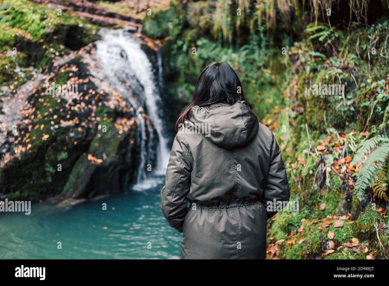 Chica en una chaqueta junto a la cascada. Otoño o invierno en Europa. Mujer  disfrutando del clima frío y la belleza de la naturaleza salvaje al aire  libre. Estilo de vida Libertad