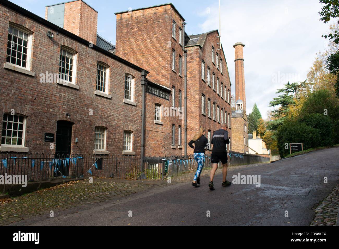 Banco de canteras Molino histórico molino de algodón 1784 , Styal, Cheshire, Reino Unido. Día de otoño con pareja corriendo colina arriba Foto de stock