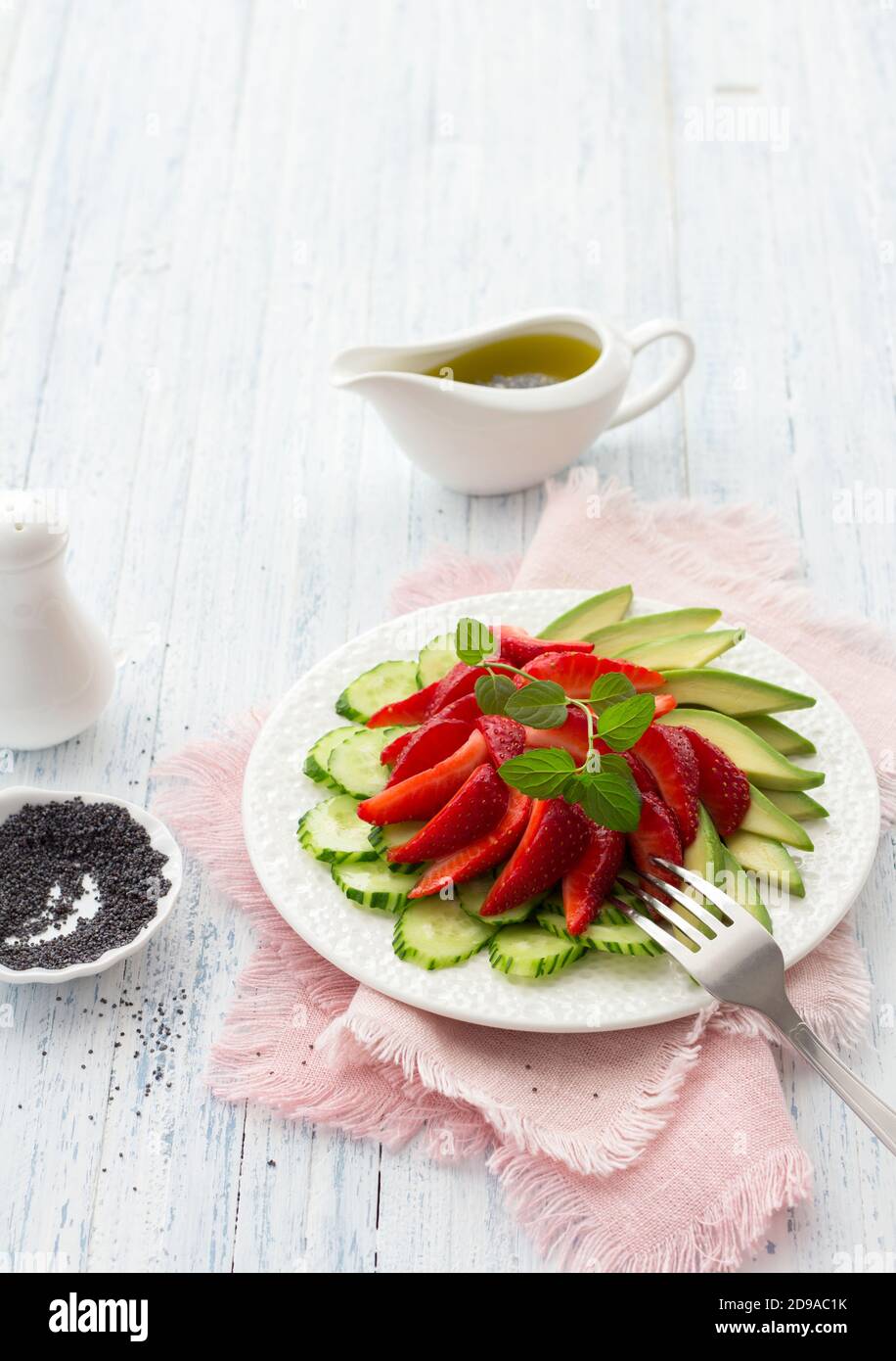Ensalada vegana de fresa, pepino y aguacate con semillas de amapola, aderezo de aceite y menta. Alimentos frescos, saludables y dietéticos. En un plato blanco y en un blu Foto de stock