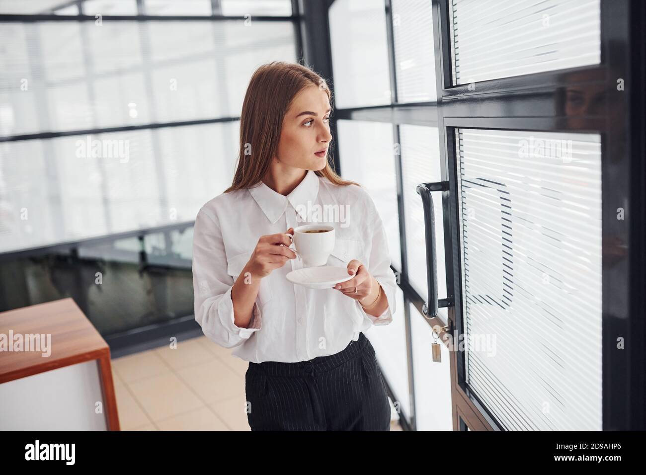 Mujer trabajadora de oficina en ropa formal de pie en el interior durante  el día con una taza de bebida Fotografía de stock - Alamy