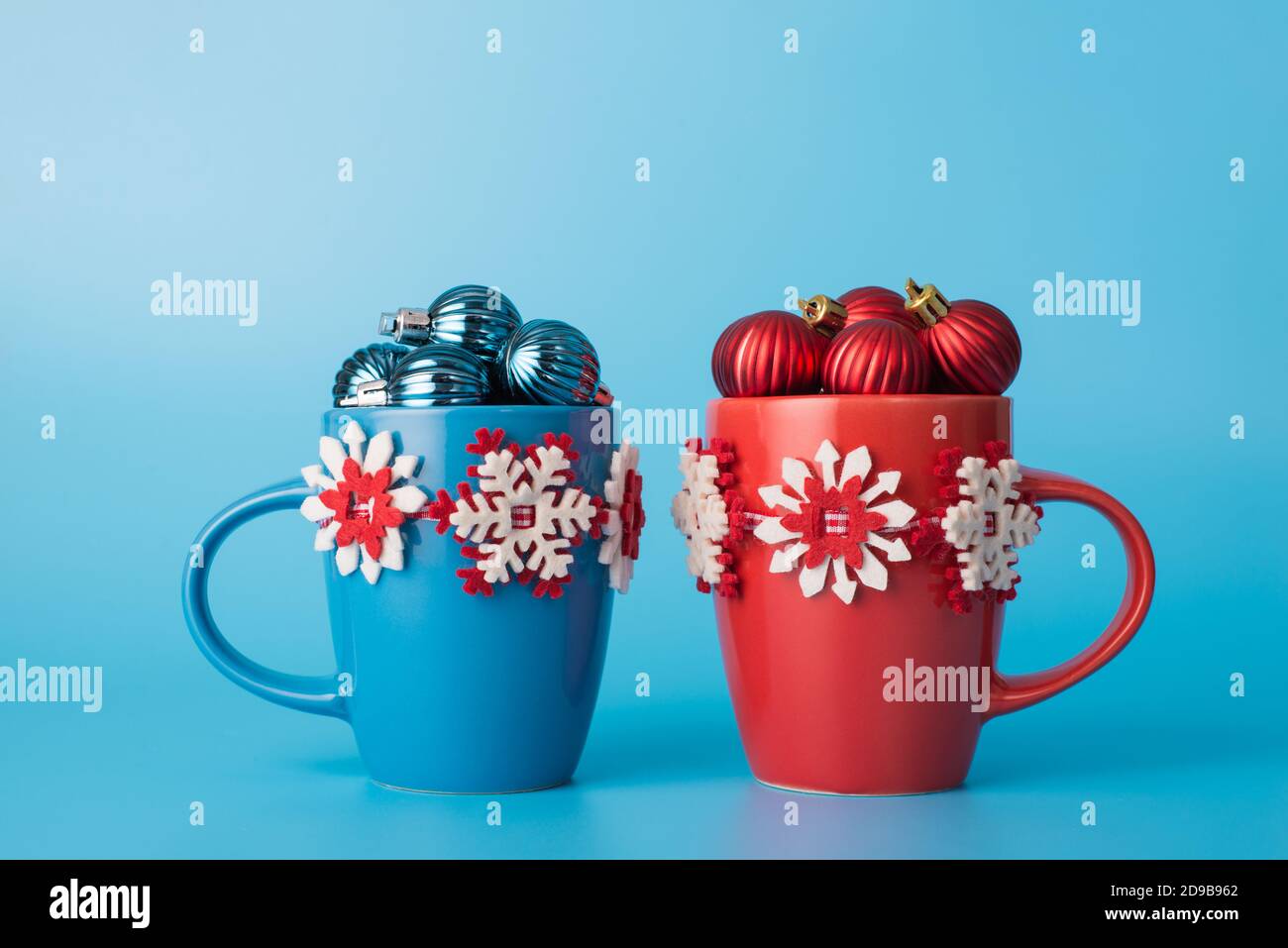 Feliz Navidad composición concepto. Primer plano foto de dos creativos con guirnalda de año nuevo tazas brillantes lleno de pequeños juguetes aislados sobre color pastel blu Foto de stock