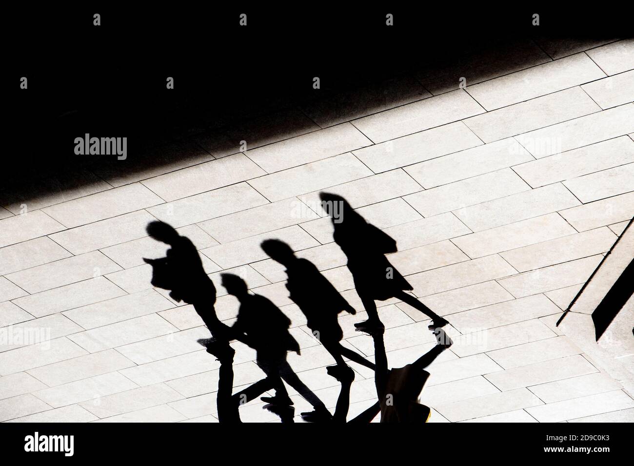 Resumen fondo sombra silueta de cuatro personas caminando pavimento de la ciudad, en alto contraste negro y blanco Foto de stock