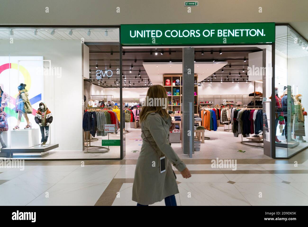 Una mujer caminando frente a la tienda de los colores Unidos de Benetton  durante el estado de alarma en el centro comercial Osito la Eliana  Fotografía de stock - Alamy