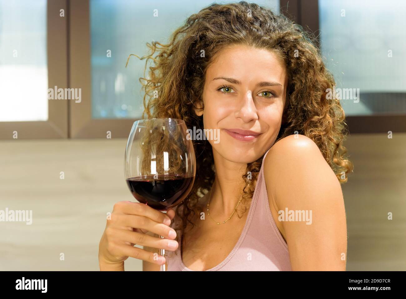 Mujer joven atractiva y amable con una sonrisa encantadora y cálida al tostar la cámara con una gran y elegante copa de vino tinto para celebrar en un retrato de primer plano Foto de stock