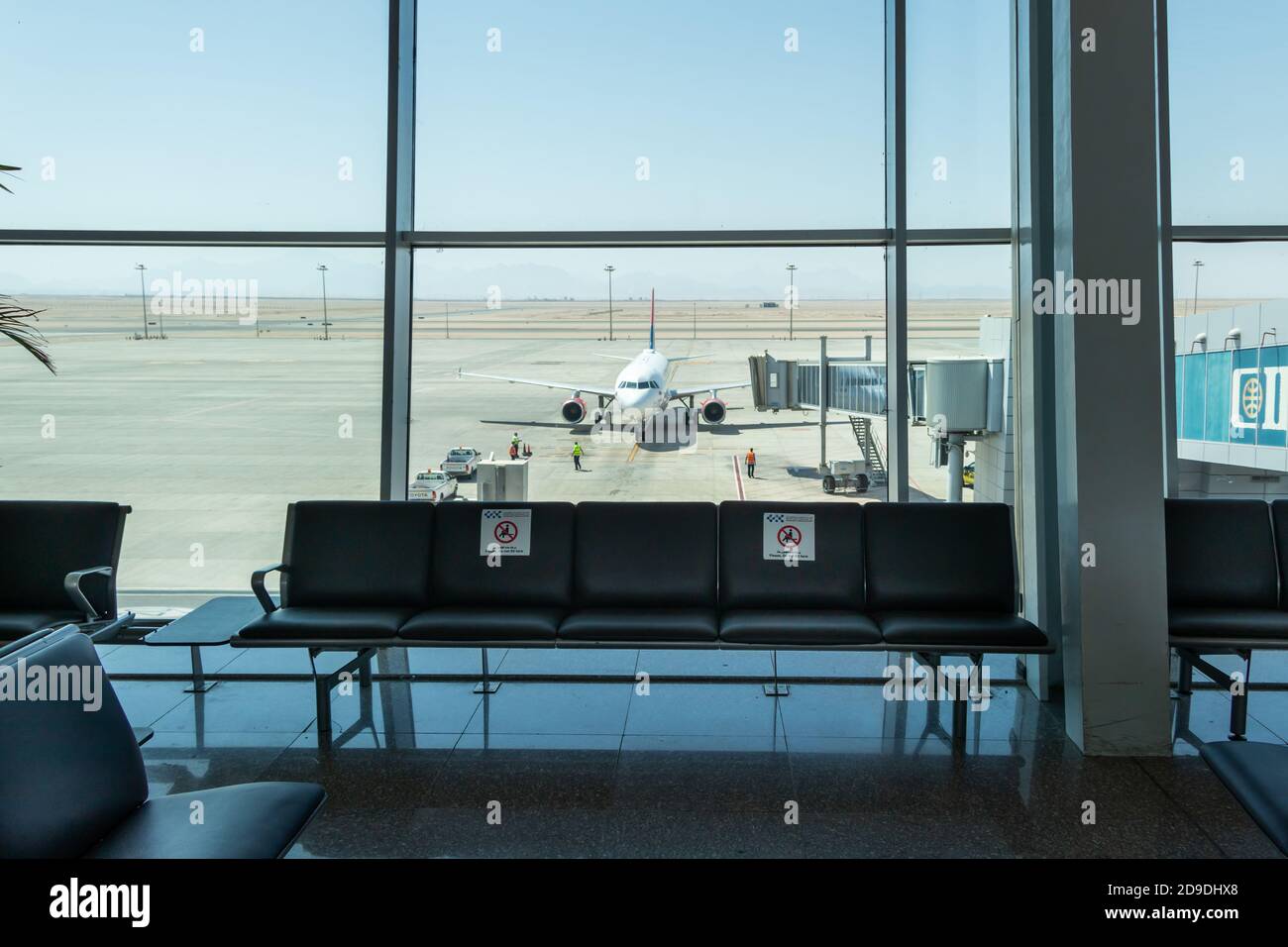 Hurghada, Egipto - 3 de octubre de 2020: Una terminal vacía con pegatinas de símbolos en las sillas. El personal del aeropuerto prepara el avión para el despegue. Viaje bajo Covid Foto de stock