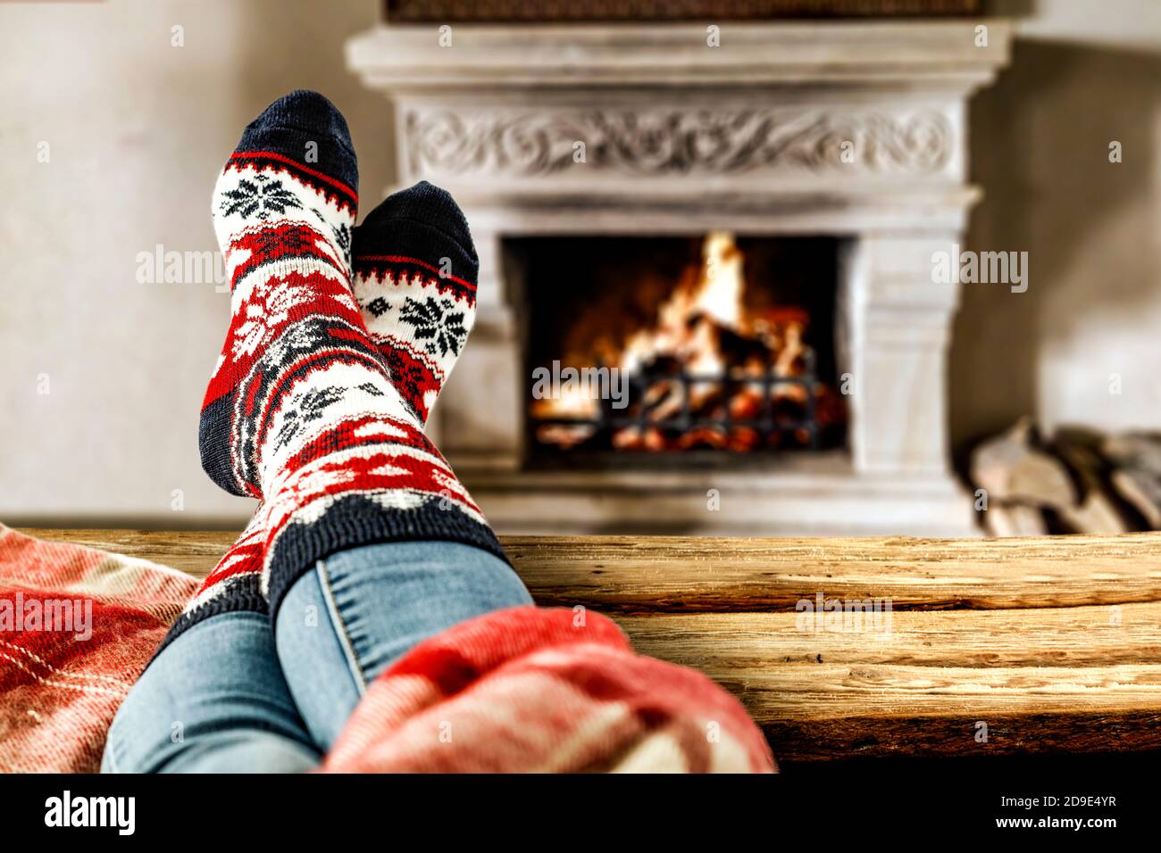 Calcetines de Navidad de lana y piernas de mujer sobre mesa de madera. Espacio para su decoración. Chimenea en el interior de la casa con luz naranja cálida de fuego.espacio de copia Foto de stock