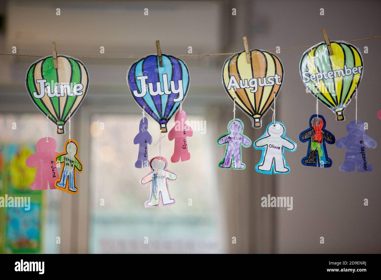 Los dibujos recortados y coloreados de globos de aire caliente con los  meses de verano escritos en ellos tienen perfiles de personas y los nombres  de los niños colgados de ellos para