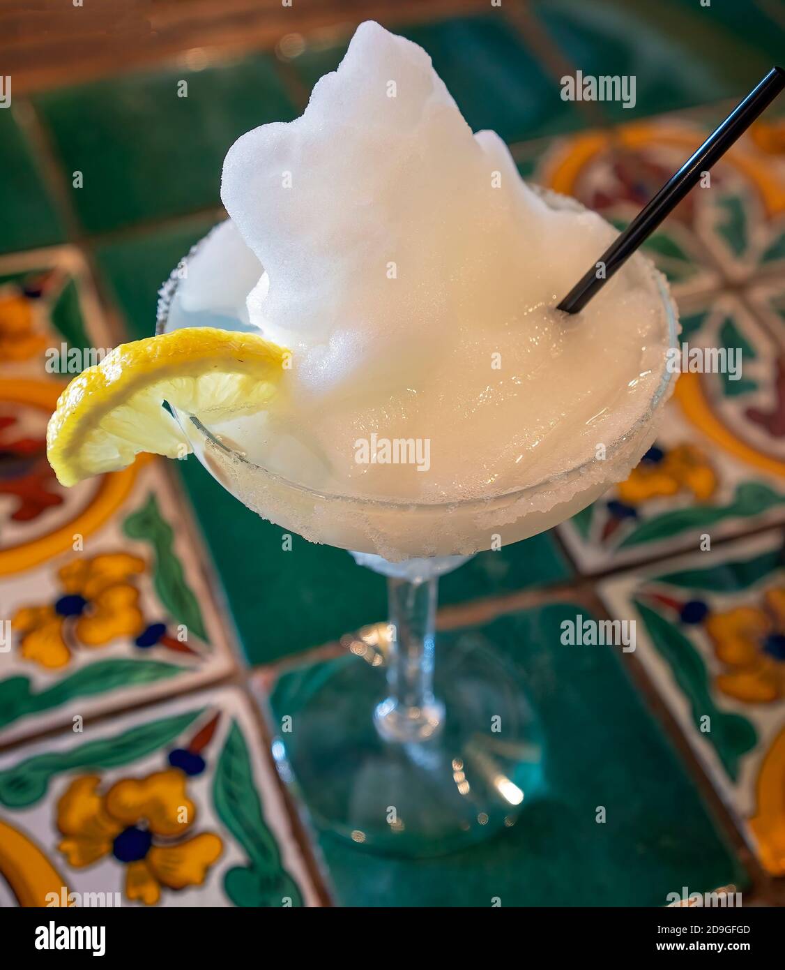 Un cóctel de tequila margarita helado paja un trozo limón en un cristal con borde de sal sentado en un decorativo mesa en un restaurante de stock -