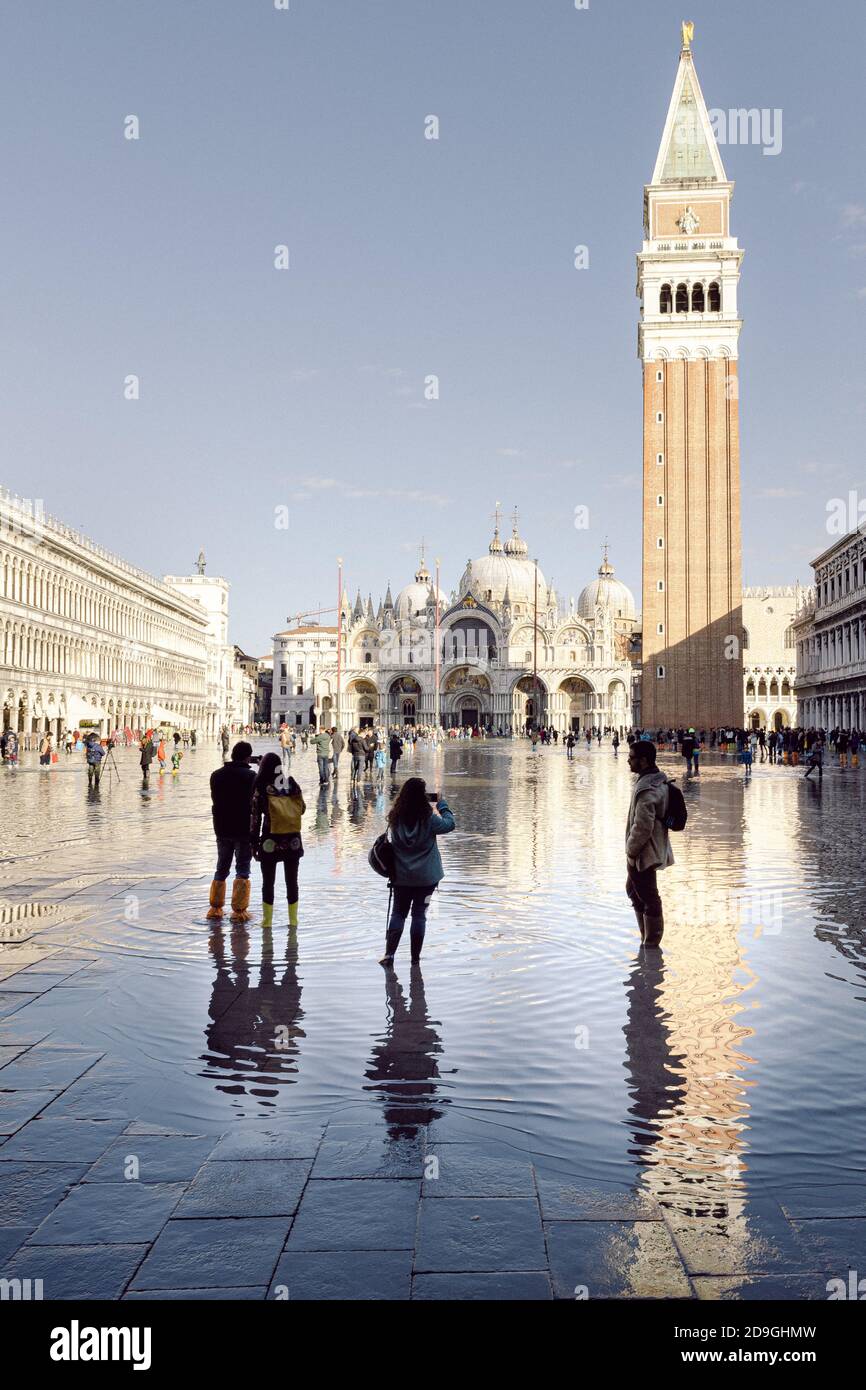 Turistas tomando fotografías en la Piazza San Marco con marea alta, acqua alta. La Basílica de San Marcos y el campanario se reflejan en el agua. Foto de stock
