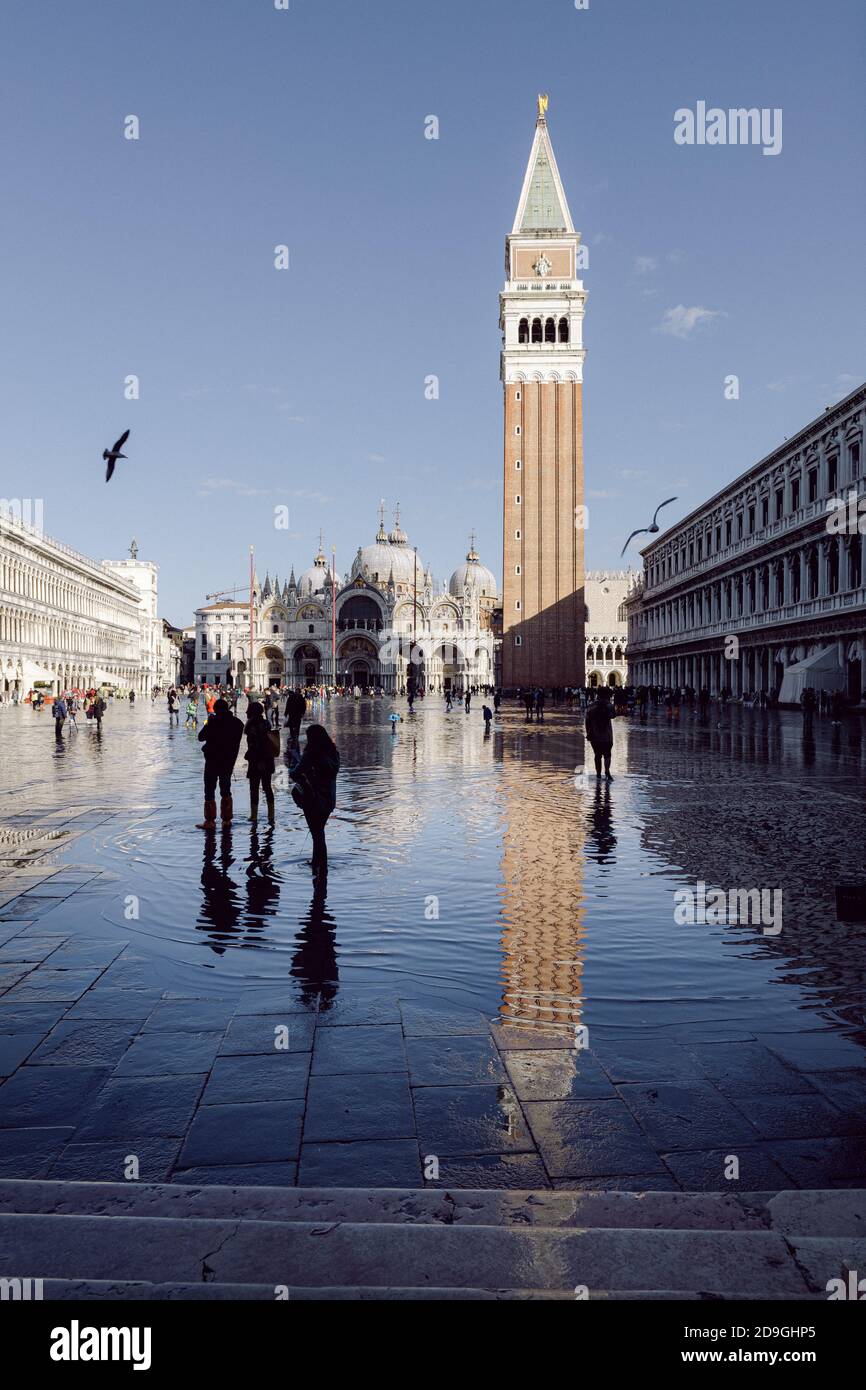 Turistas tomando fotografías en la Piazza San Marco con marea alta, acqua alta. La Basílica de San Marcos y el campanario se reflejan en el agua. Foto de stock