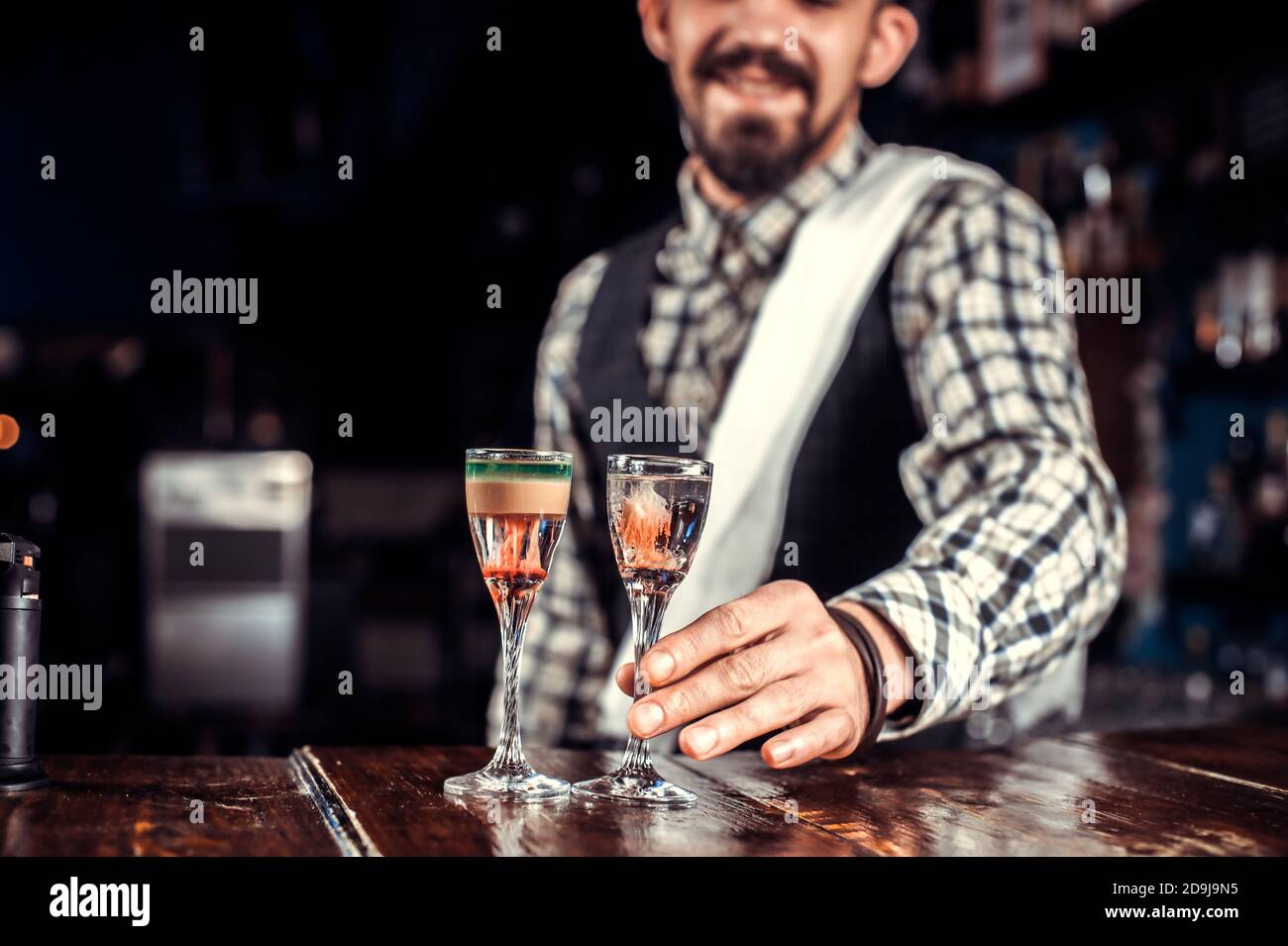 El barman profesional decora la mezcla de colores mientras está de pie cerca del bar contador en el bar Foto de stock