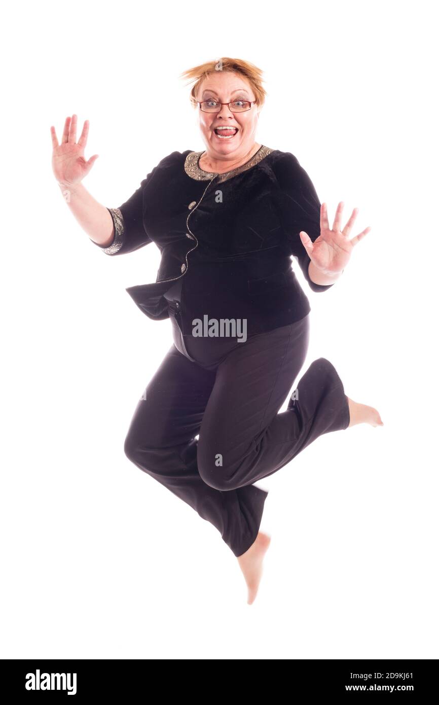 Mujer de mediana edad con chaqueta negra y pantalones saltando, retrato de estudio sobre fondo blanco Foto de stock