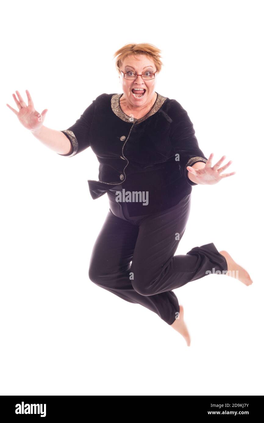 Mujer de mediana edad con chaqueta negra y pantalones saltando, retrato de estudio sobre fondo blanco Foto de stock