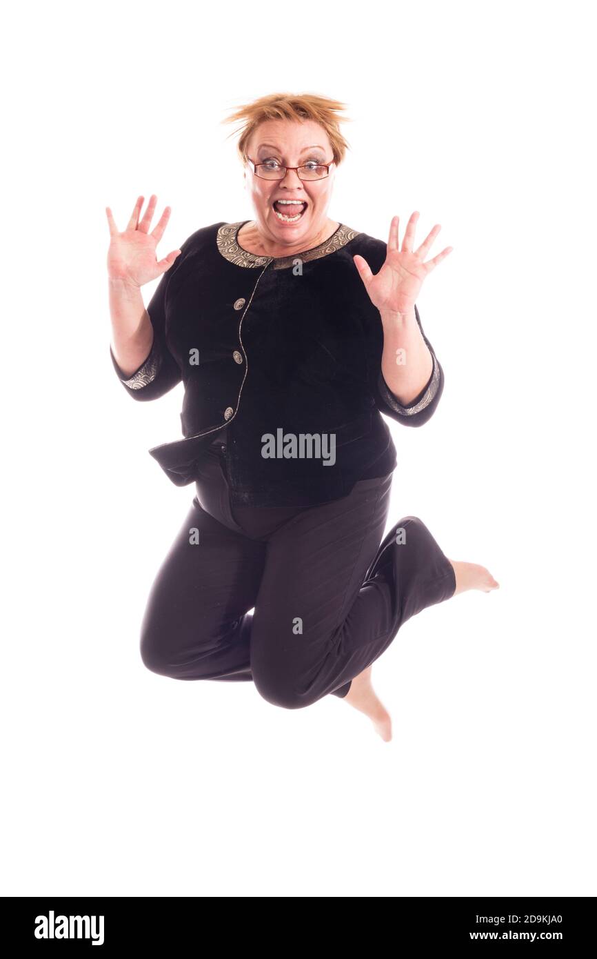 Mujer de mediana edad con chaqueta negra y pantalones saltando, retrato de estudio sobre fondo blanco Foto de stock