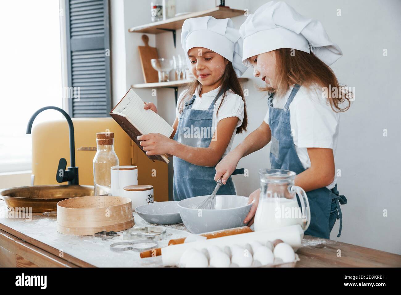 Dos niñas en uniforme azul chef preparando la comida la cocina y leer el libro de recibos Foto de stock