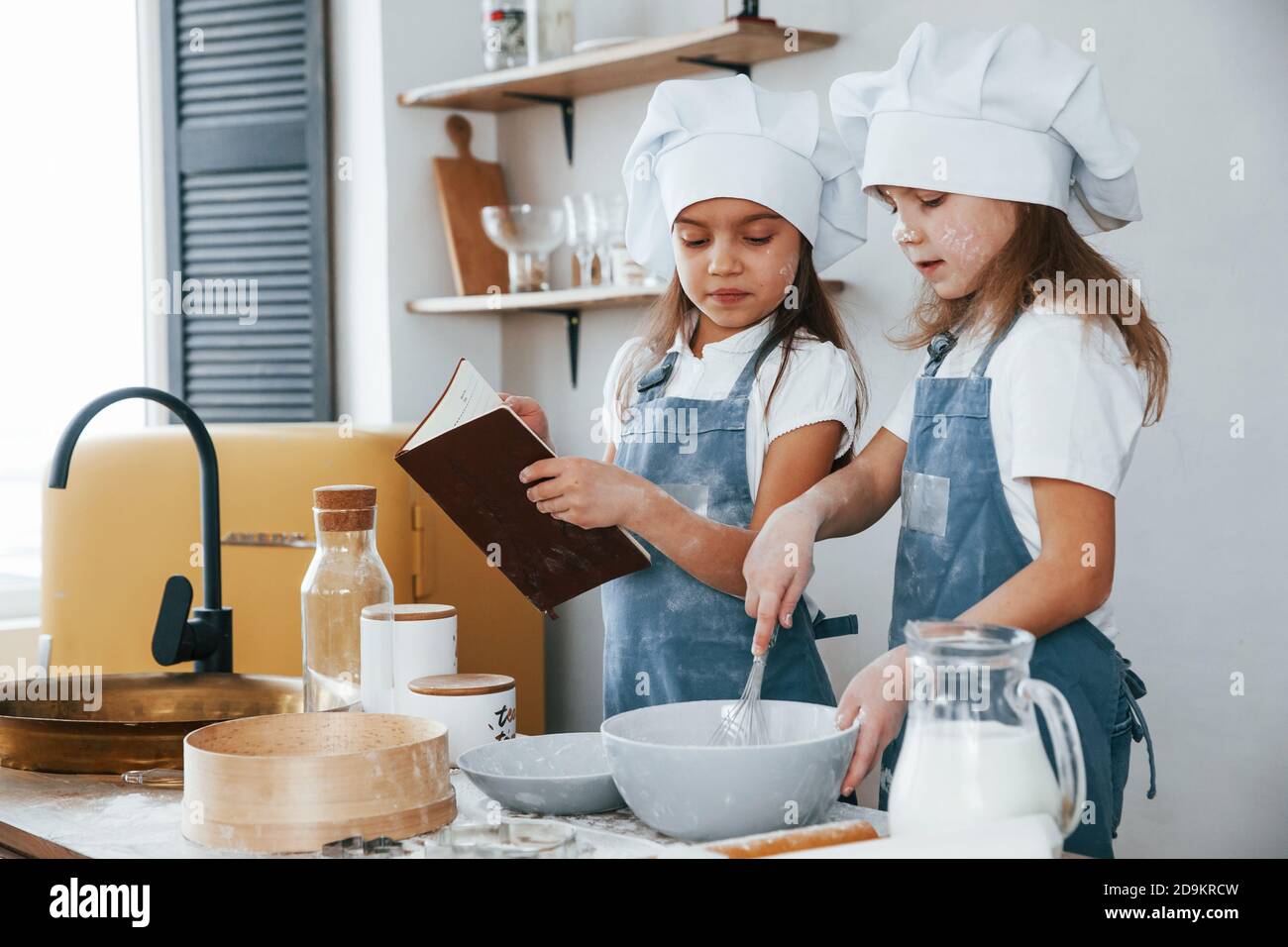 Dos niñas en uniforme azul chef preparando la comida la cocina y leer el libro de recibos Foto de stock