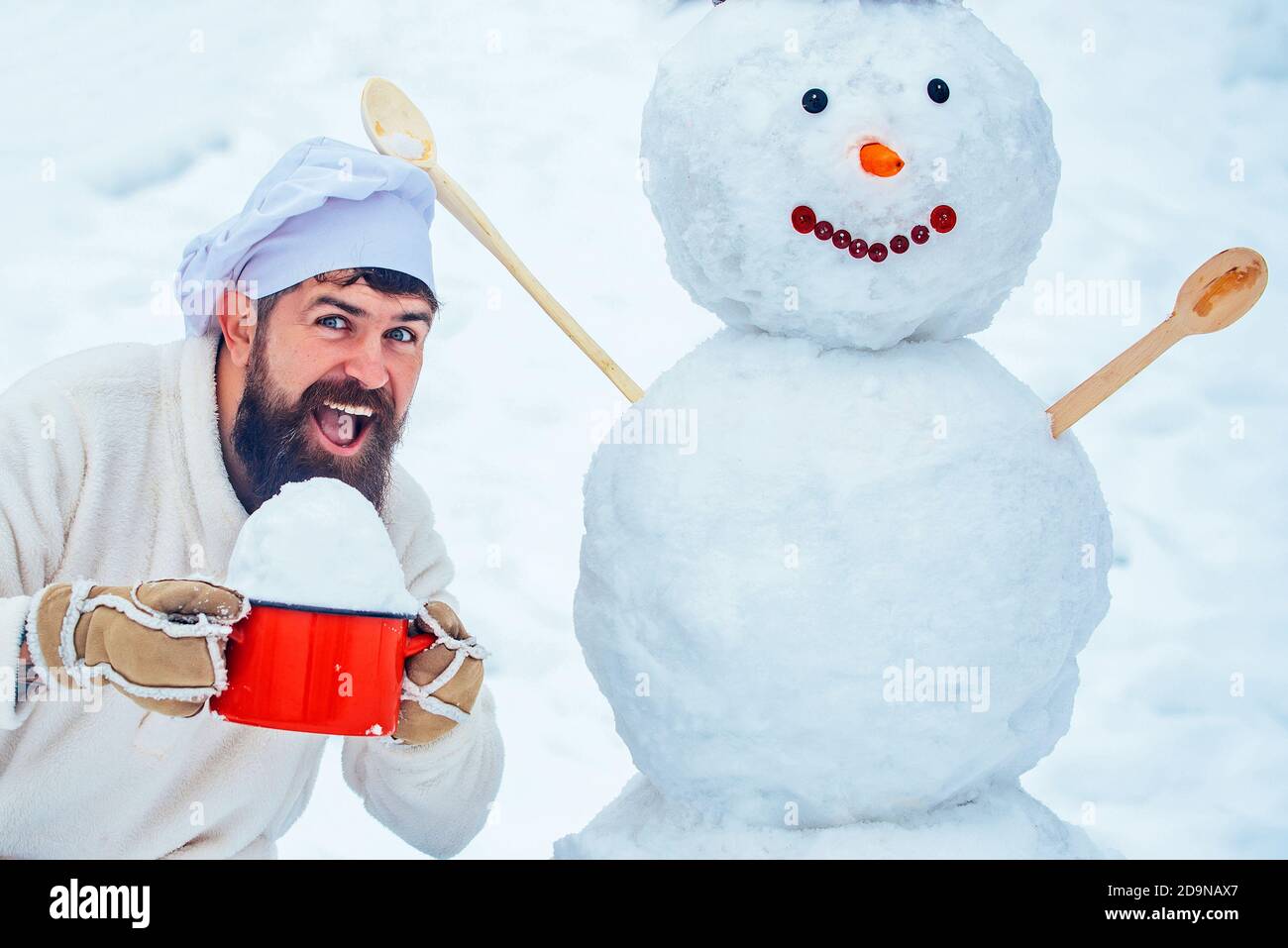 Cocina de Navidad. Divertido cocinero de Navidad. Feliz padre chef jugando  con un muñeco de nieve en una caminata de invierno nevado. Papá Noel  cocinero desea Feliz Navidad Fotografía de stock -