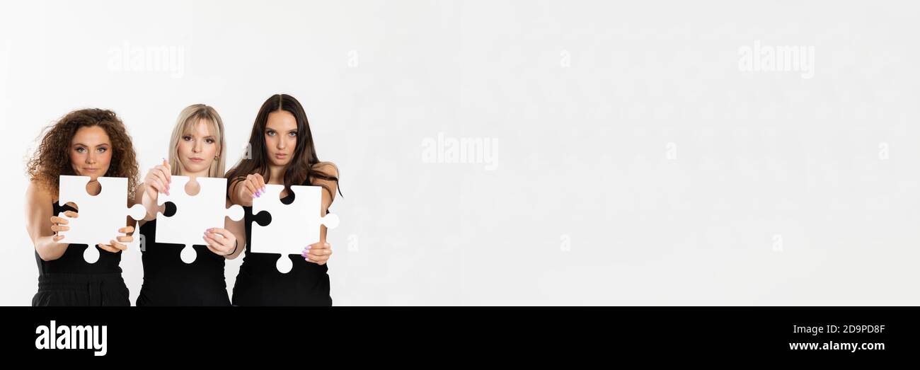 Largo panorama con espacio para una descripción con las niñas de diferentes razas con piezas de rompecabezas en la mano. Las mujeres firmes en su mensaje al mundo. Foto de stock