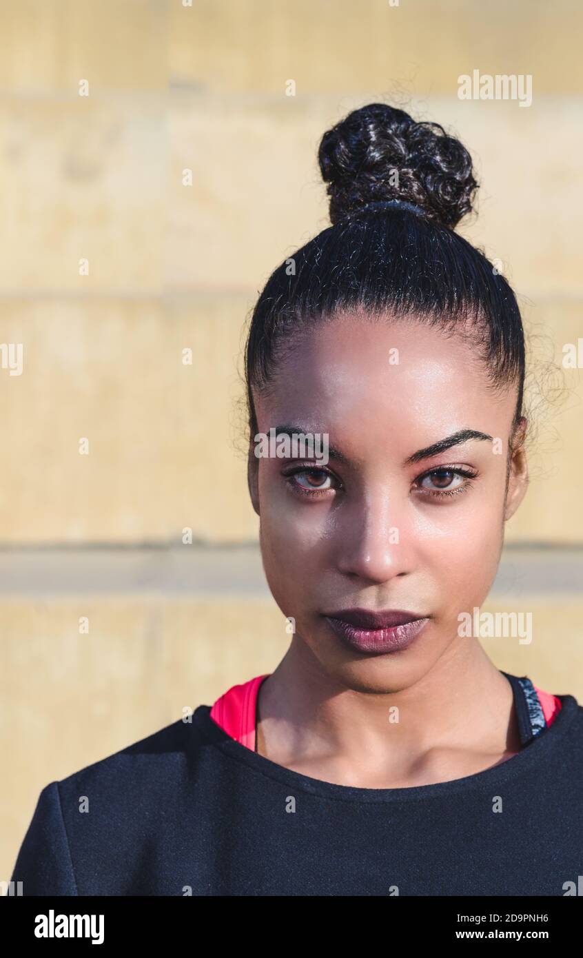 Retrato vertical de atractiva joven afroamericana con cabello atado de vuelta en un ponytail usando sportswear y mirando seriamente la cámara Foto de stock