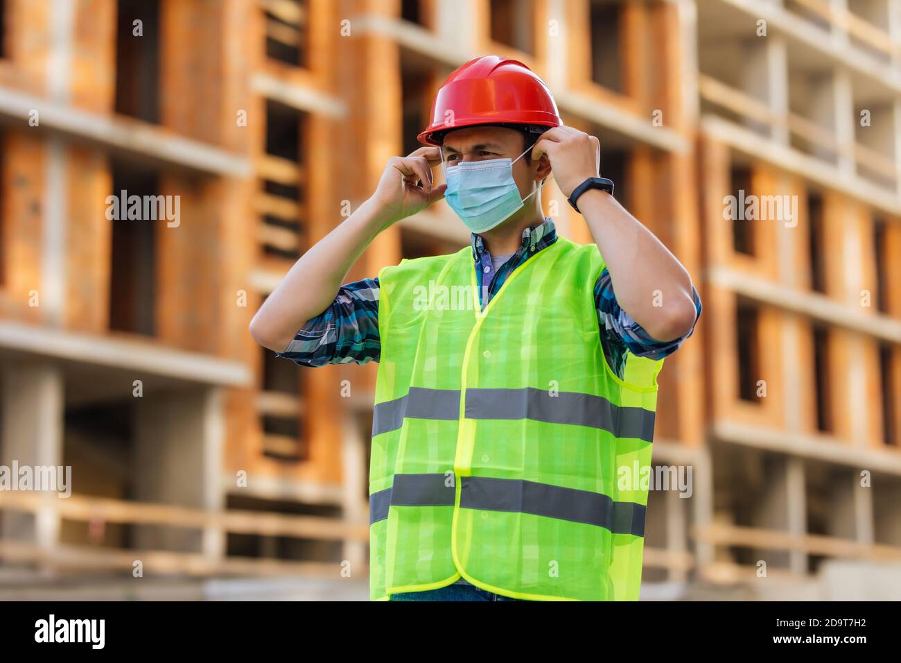 Ingeniero en casco de protección y máscara médica en el sitio de construcción durante la epidemia de coronavirus Foto de stock