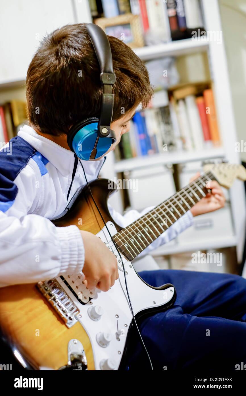 niño tocando la guitarra eléctrica en casa con un par de auriculares y una  biblioteca sin enfoque en el fondo, enfoque selectivo, encuadre vertical  Fotografía de stock - Alamy