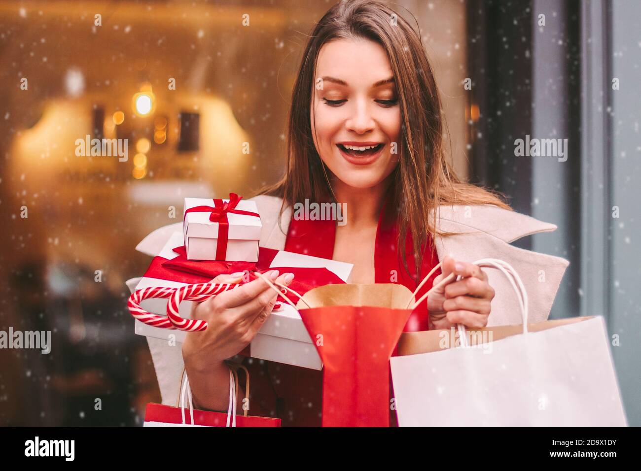 Feliz hermosa chica emocionada mirar en la bolsa de compras y sonreír en la  calle nevada de invierno. Alegre joven atractiva mujer sostener bolsas de  papel y cajas de regalo i Fotografía