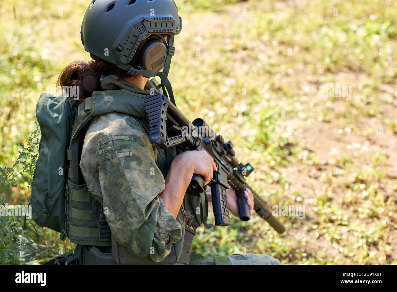 vista lateral sobre una mujer irreconocible con ropa militar sentada en el césped esperando al al lado, a disparar Fotografía de stock - Alamy