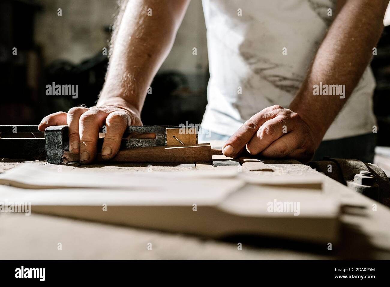 Trabajador de madera macho de cultivo de pie en el banco de trabajo antiguo y trabajando con detalles de madera en un taller de rallones Foto de stock