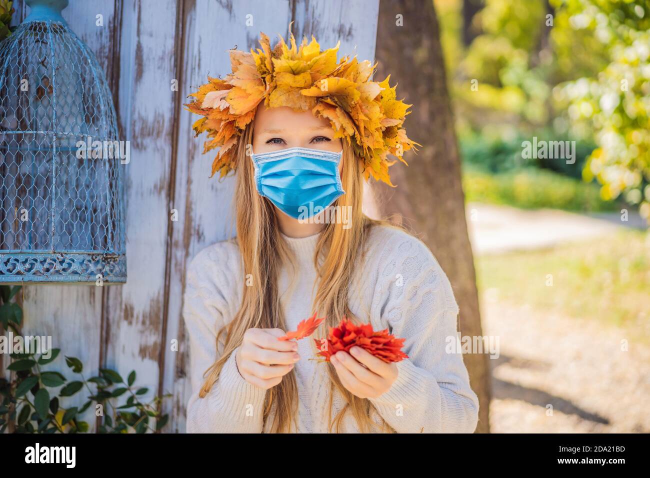 Estilo de vida al aire libre primer plano retrato de encantadora mujer joven rubia Usar una máscara médica durante el coronavirus COVID-19 usando una corona de otoño Foto de stock