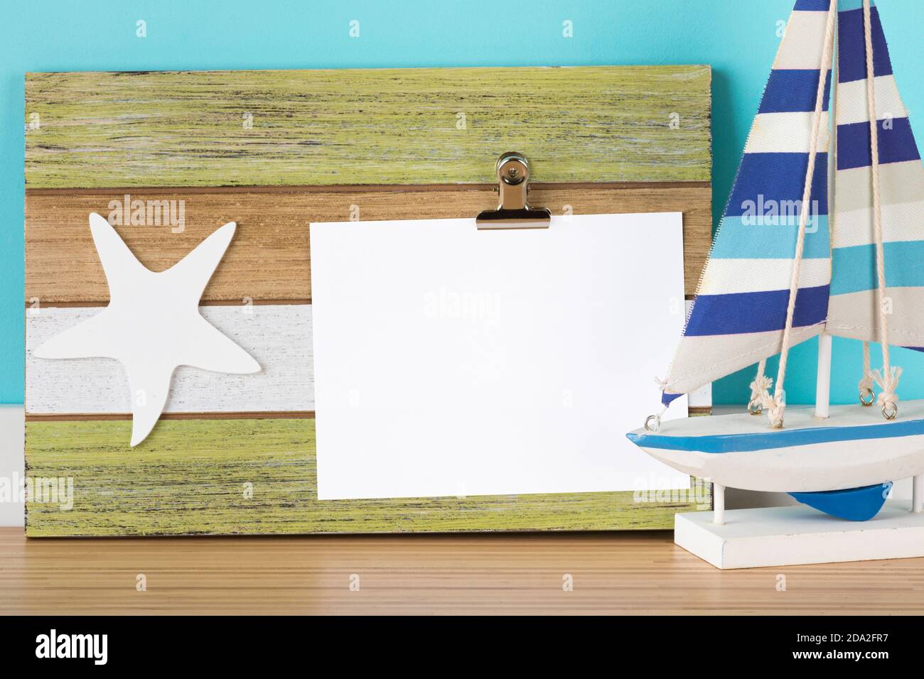 Careta de felicitación mockup en rústica portapapeles de madera. Decoración marítima con ornamento de estrella de mar y barco de vela de juguete. Área en blanco enmascarada con trazado de recorte Foto de stock