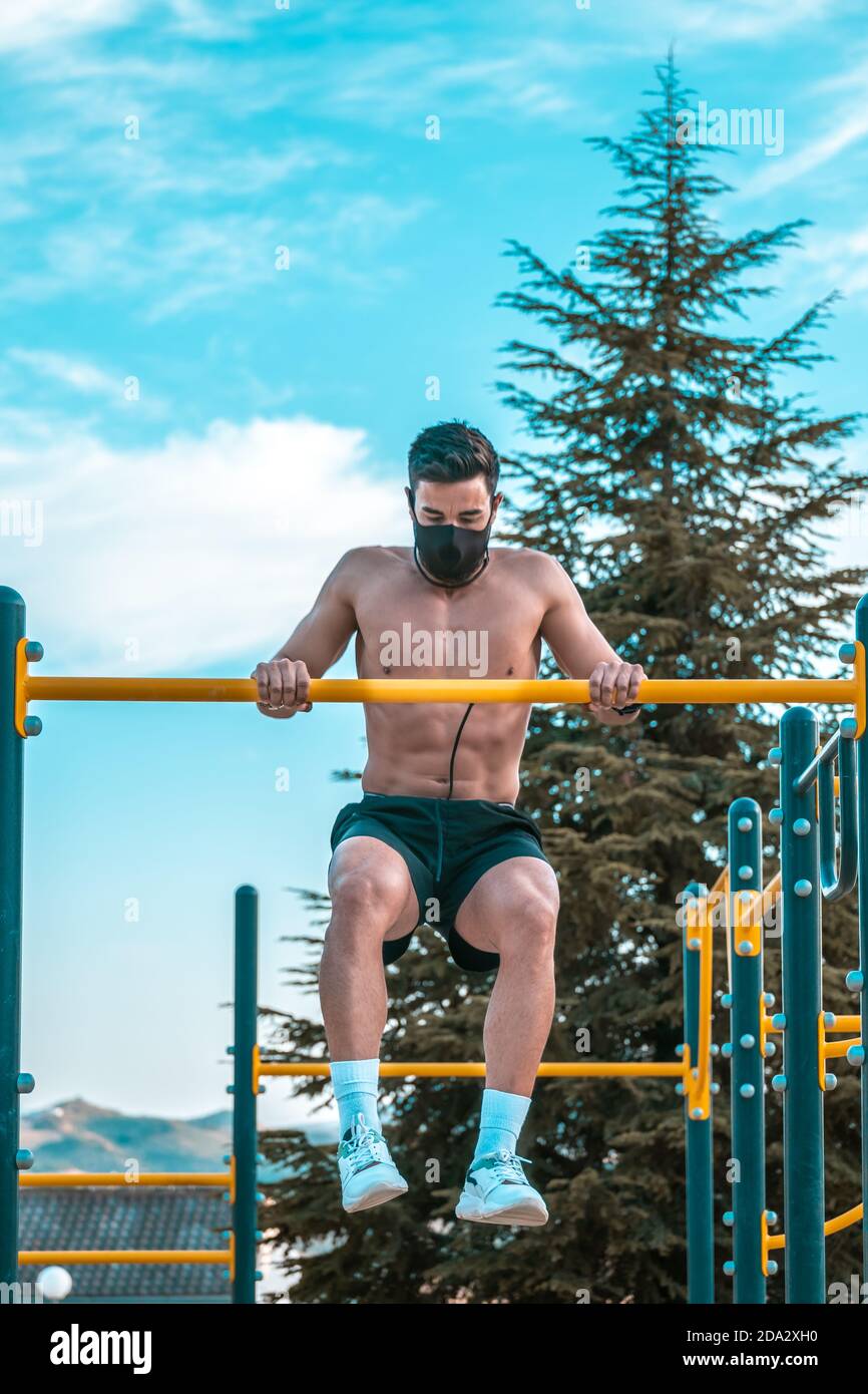 Joven latino sin camisa y pantalones negros y. máscara haciendo pull-ups en  un bar del parque calistenics Fotografía de stock - Alamy