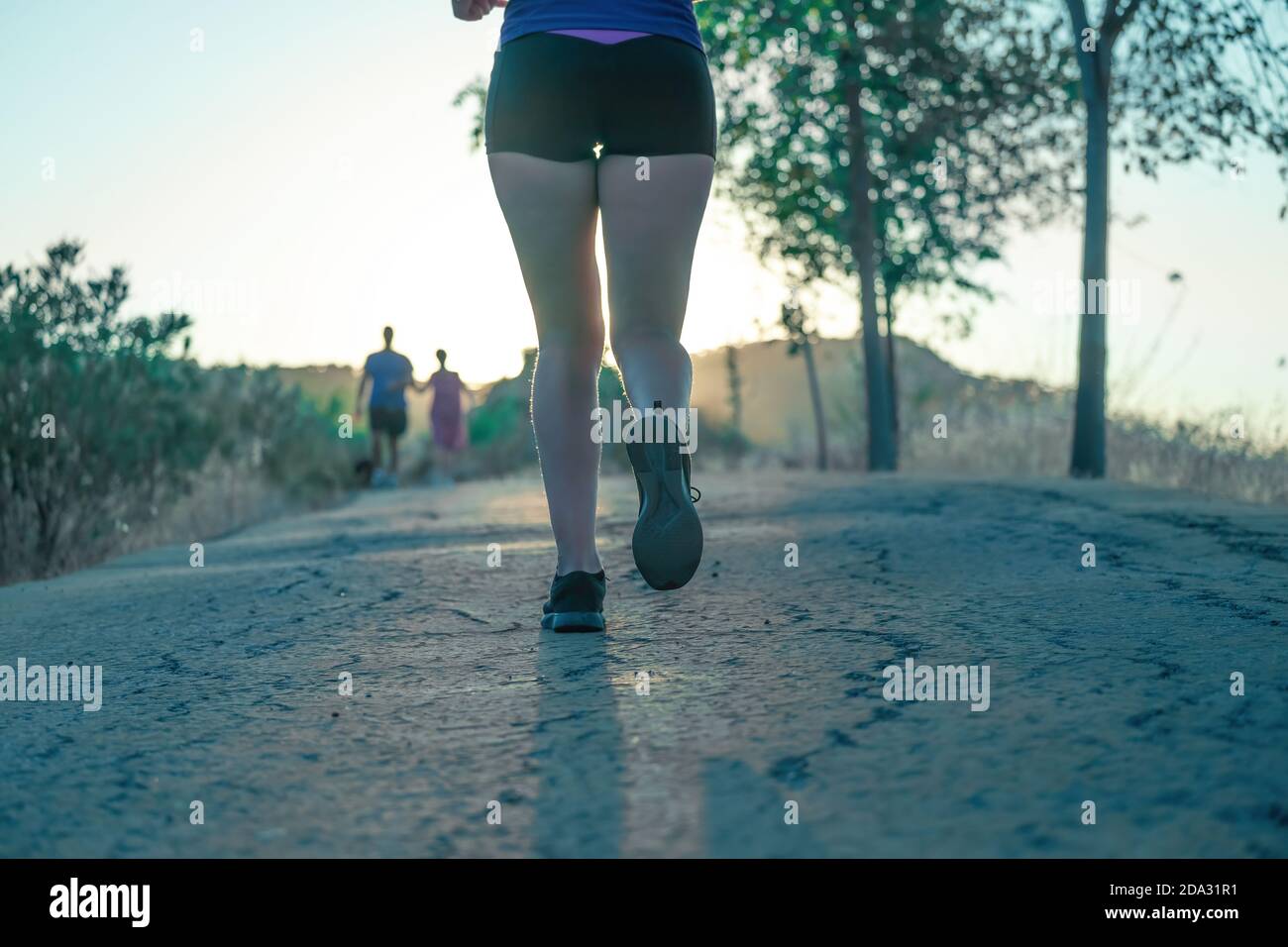 Foto retroiluminada de las piernas de la mujer joven corriendo por el parque por la tarde Foto de stock