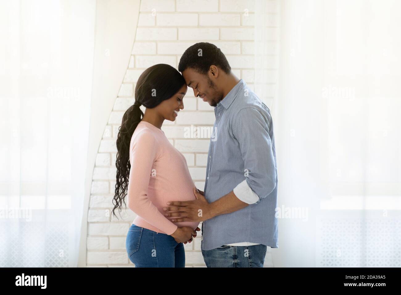 Hombre negro guapo tocando el vientre de su esposa embarazada en el interior, vista lateral Fotografía de stock foto