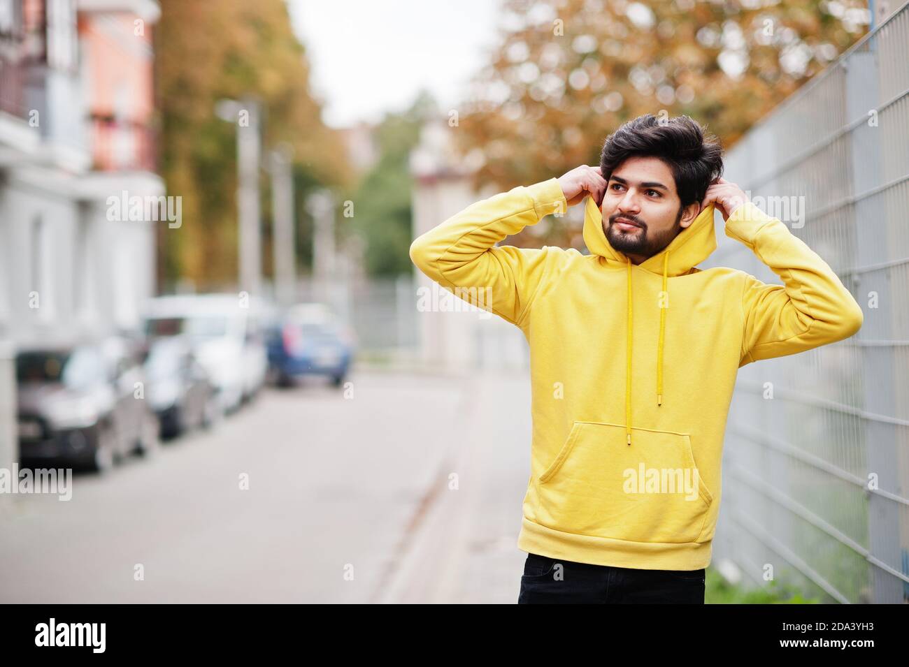 Joven hipster urbano hombre indio en una moderna sudadera amarilla