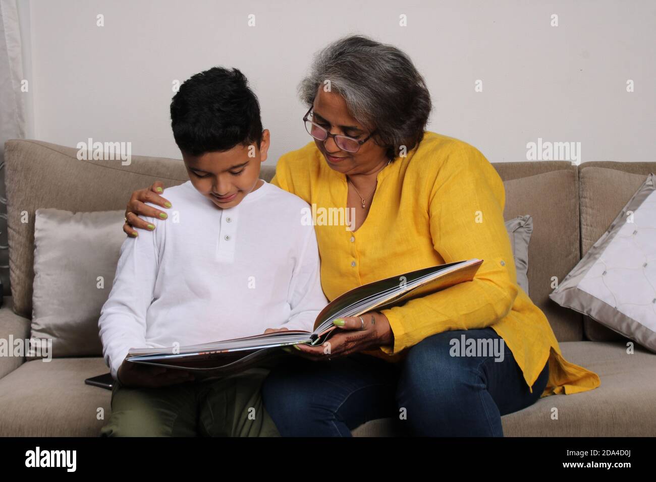 Momentos felices con la abuela, la señora mayor india/asiática pasando tiempo de calidad con su gran hijo leyendo libro juntos. Foto de stock