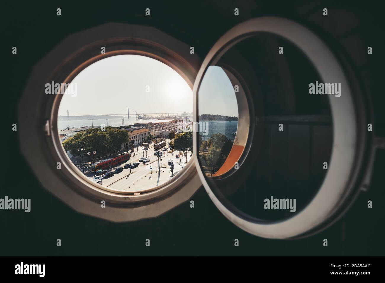 Vista a través de una ventana abierta redonda de un antiguo edificio  histórico de un paisaje de Lisboa con una animada plaza con tranvía,  autobús, y coches, un puente Fotografía de stock -