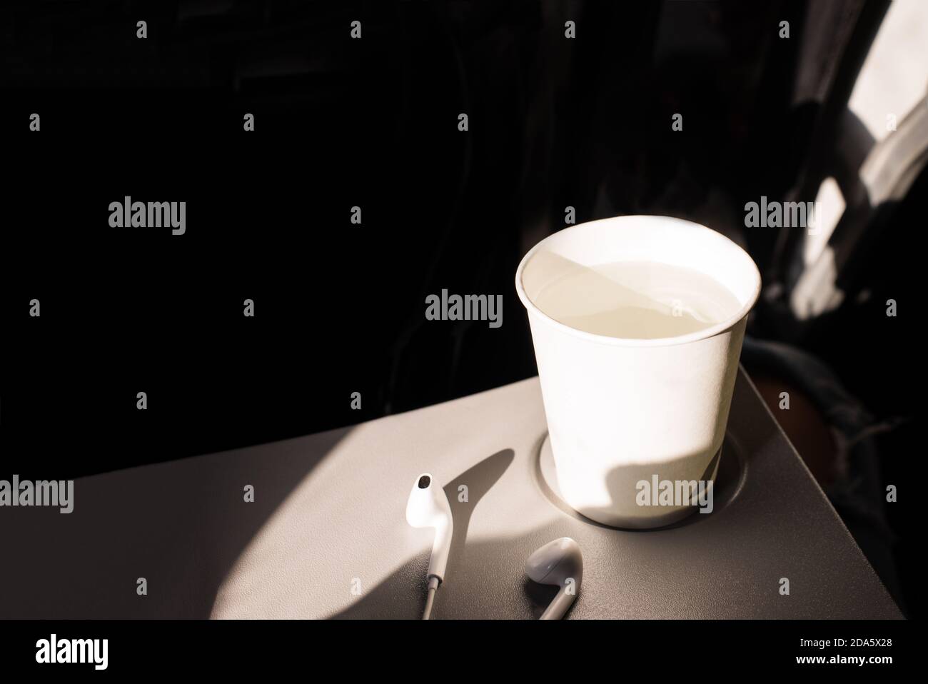 Taza de papel blanco de agua y auriculares en una mesa plegable en un avión.  Bebidas en el avión. Deshidratación en vuelo. Hidratación de la piel  Fotografía de stock - Alamy