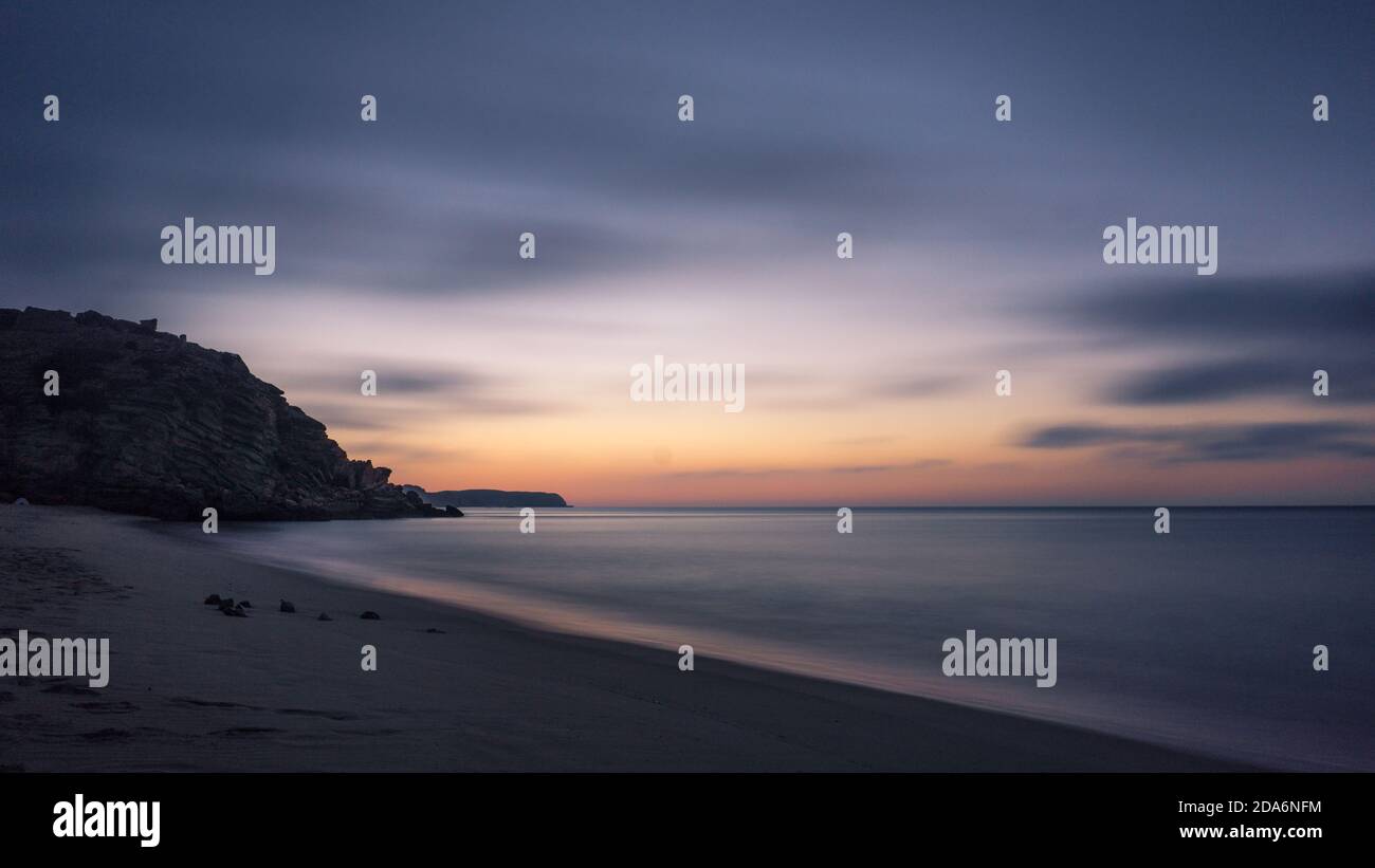 Larga exposición de una puesta de sol con colorido paisaje marino del cielo en Playa Figueira en Portugal Foto de stock