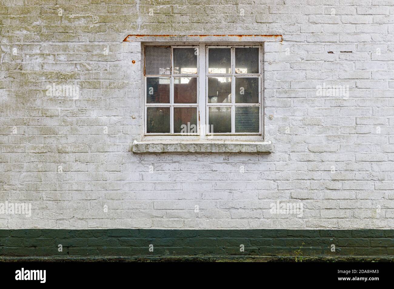 Textura de una ventana con un marco pintado de blanco y una pared de ladrillo con pintura blanca gruesa, en el fondo es una toma verde de ladrillos pintados de verde. Foto de stock