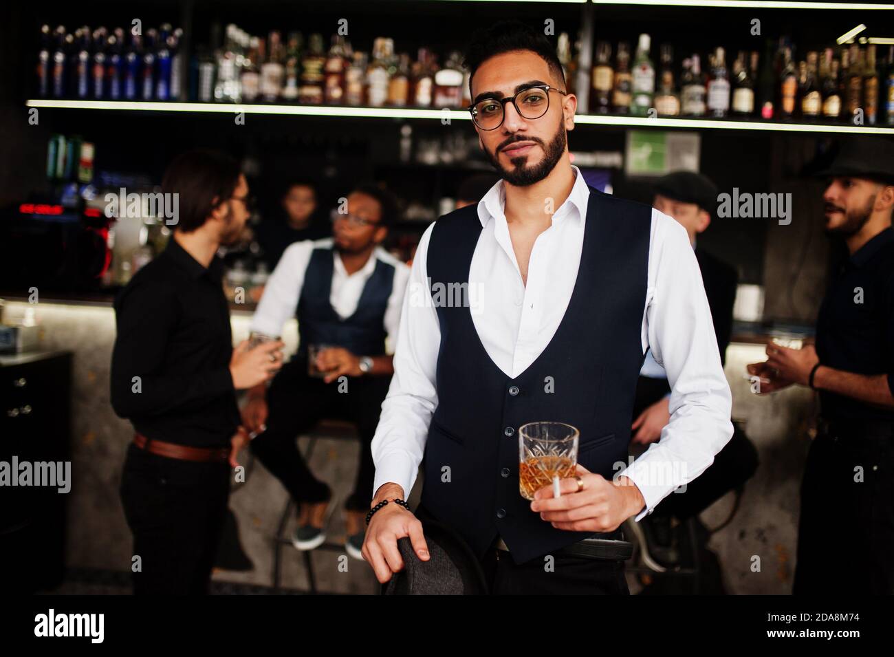Un hombre árabe con estilo contra un grupo de guapos vestidos retro y bien vestidos gángsters pasar tiempo en el club, bebiendo en el bar. Soltero multiétnico masculino Fotografía de stock - Un hombre árabe con estilo contra un grupo de guapos vestidos retro y bien vestidos gángsters pasar tiempo en el club, bebiendo en el bar. Soltero multiétnico masculino Fotografía de stock -