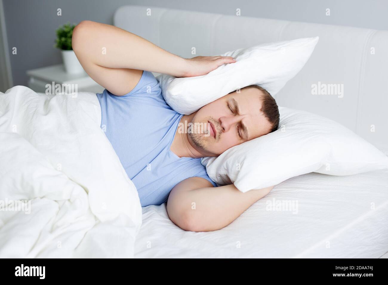 concepto de insomnio y dolor de cabeza - retrato de un joven cansado  acostarse en la cama y sostener almohadas en la cabeza Fotografía de stock  - Alamy