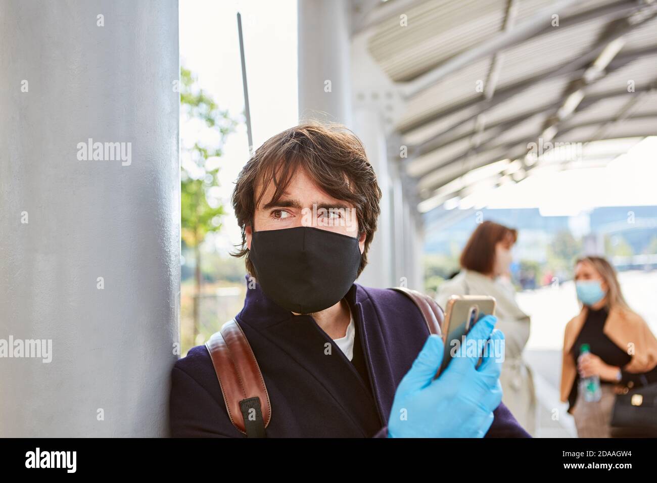 Hombre como un viajero con máscara y smartphone con advertencia Sobre Covid-19 Foto de stock