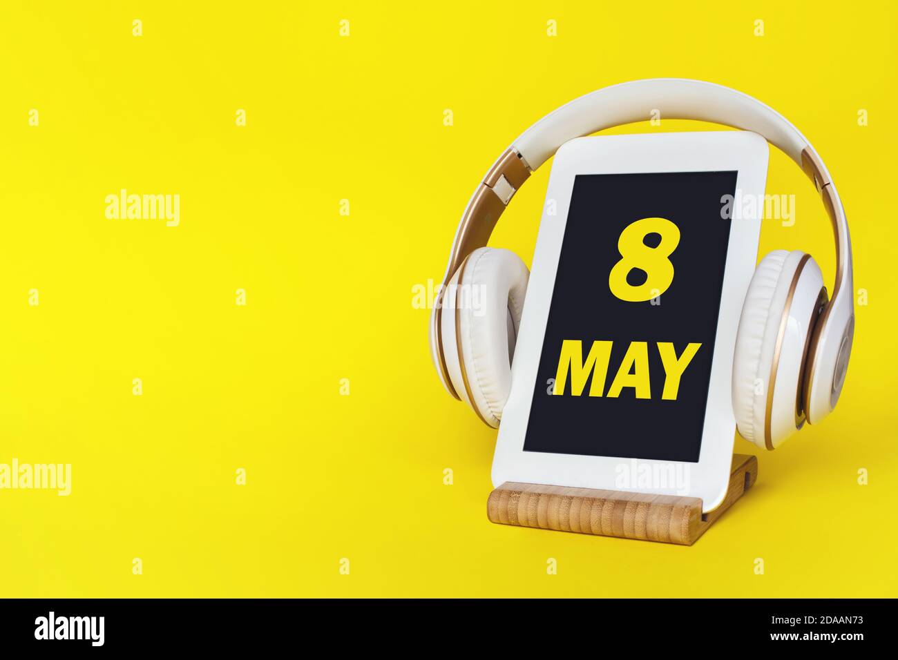 8 de mayo. Día 8 del mes, fecha del calendario. Auriculares elegantes y tableta moderna sobre fondo amarillo. Espacio para texto. Concepto de educación, tecnología, vida Foto de stock