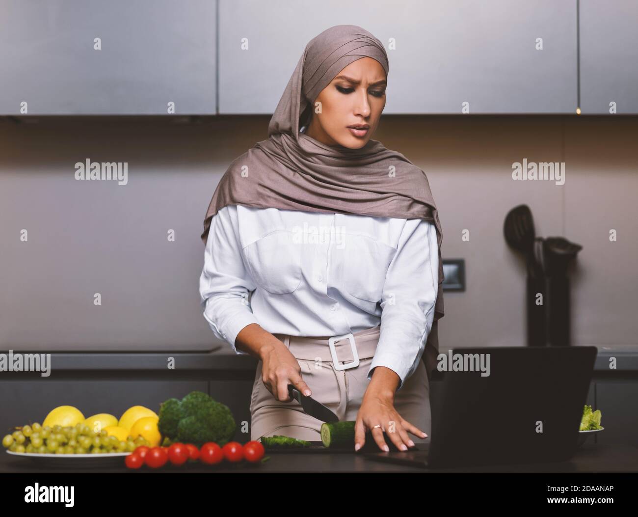 Mujer musulmana Aprendiendo a cocinar viendo videos en el interior de la computadora portátil Foto de stock